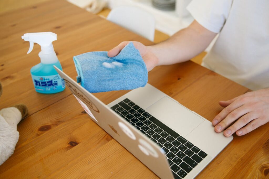 pexels-photo-4008556 Person disinfecting laptop with spray and cloth, ensuring cleanliness and hygiene indoors.