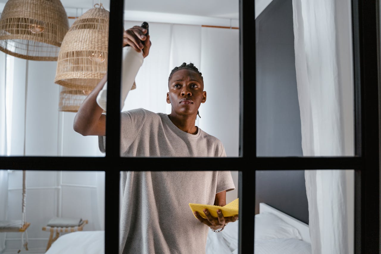 Man cleaning glass window indoors using a spray bottle and cloth.